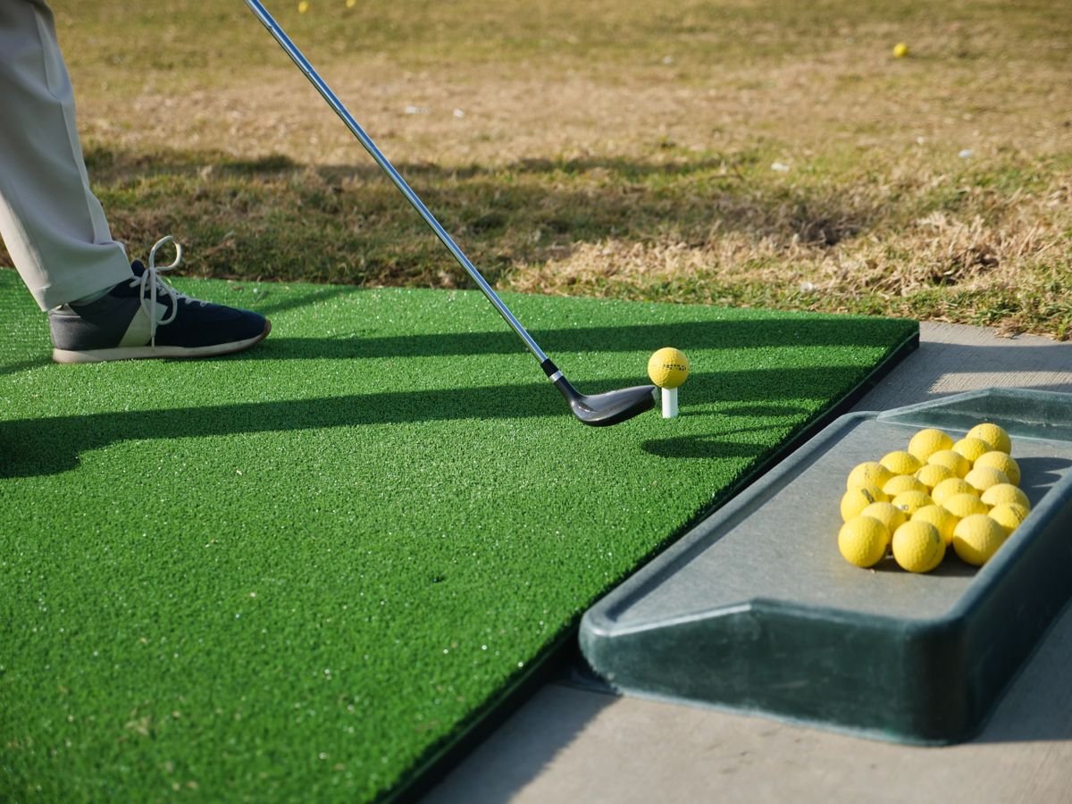 Golfer practicing with the best wooden golf alignment sticks on a driving range mat