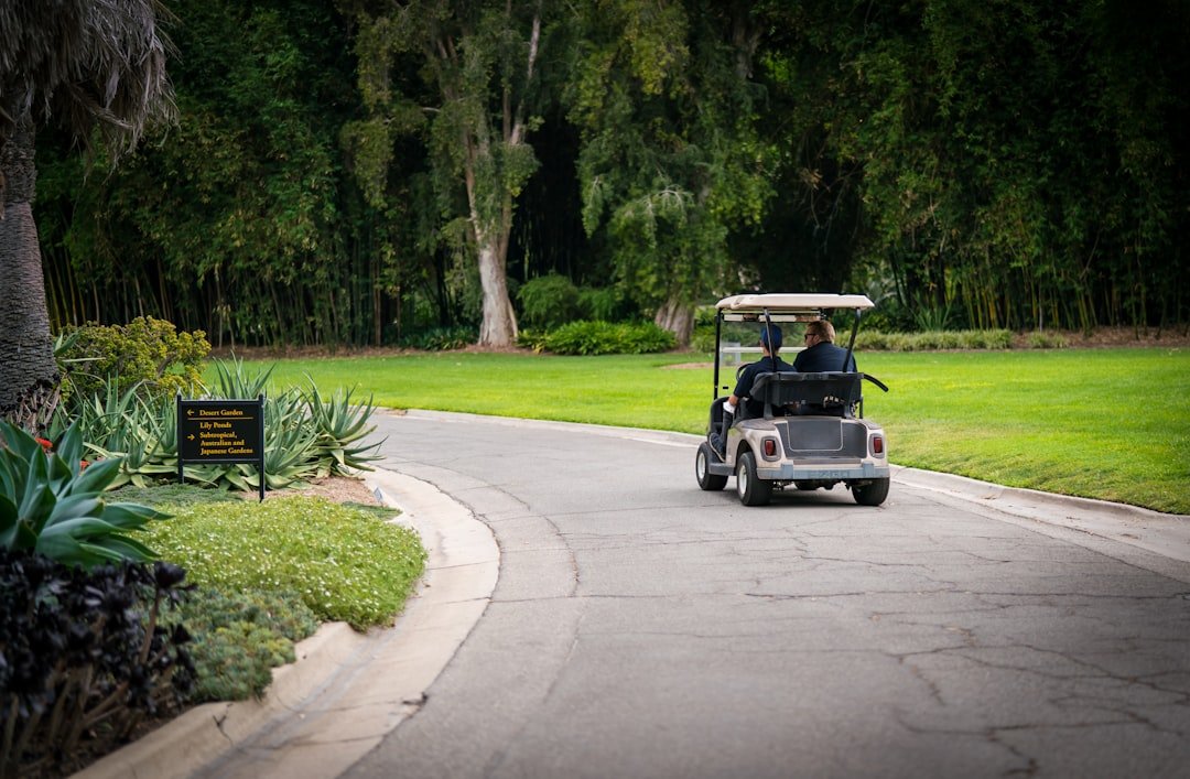 White electric golf cart driving on a paved road, powered by its onboard motor
