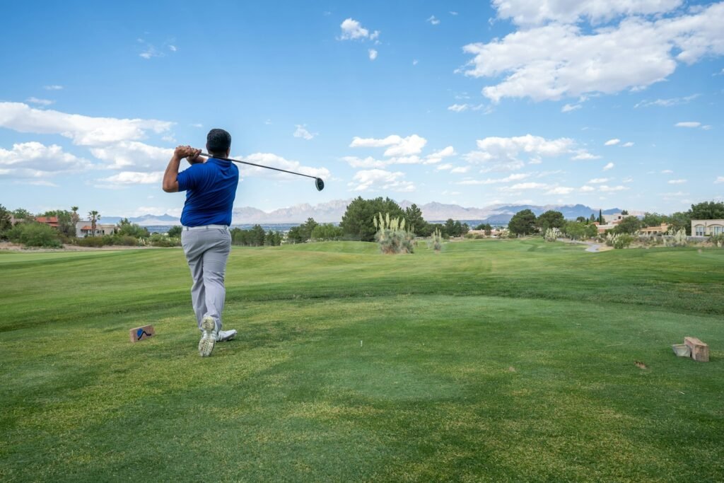 Golfer completing a full swing and follow-through while teeing off on a sunny course