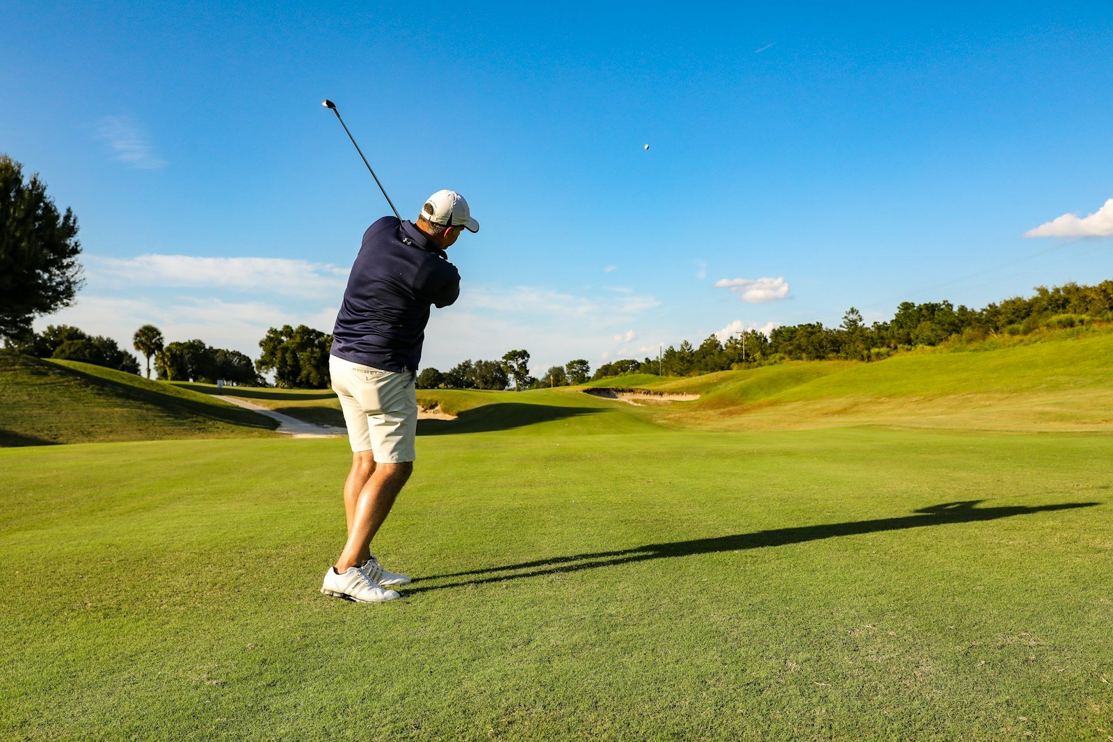 Golfer completing a full swing follow-through on a sunny golf course