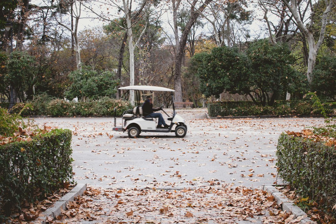 White golf cart driving through a park in autumn leaves before it is stored for winter