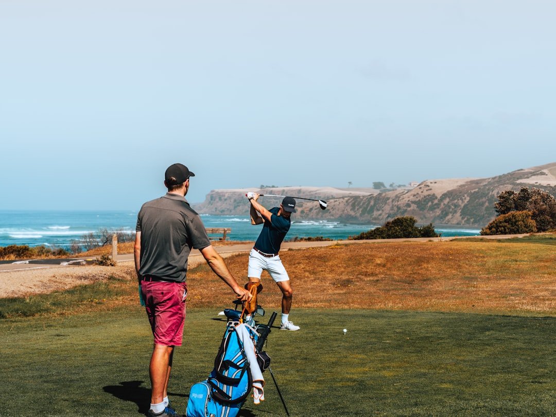 Two golfers at a scenic course, one swinging while the other watches and holds the bag