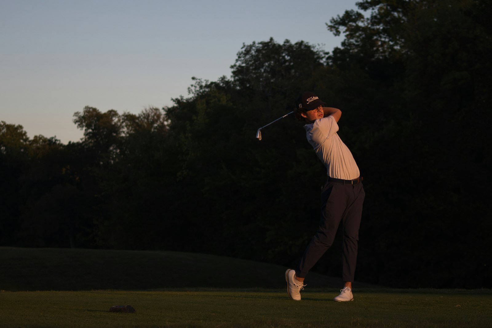 Golfer silhouetted against the evening sky finishing the follow-through of a golf swing