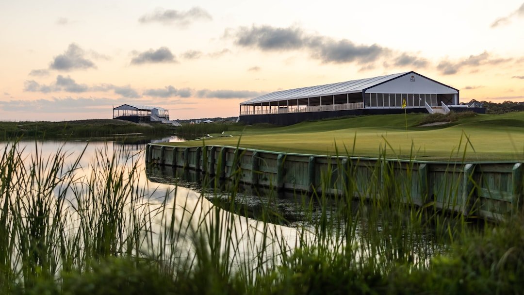 Golf clubhouse building beside a course fairway and water feature at sunset