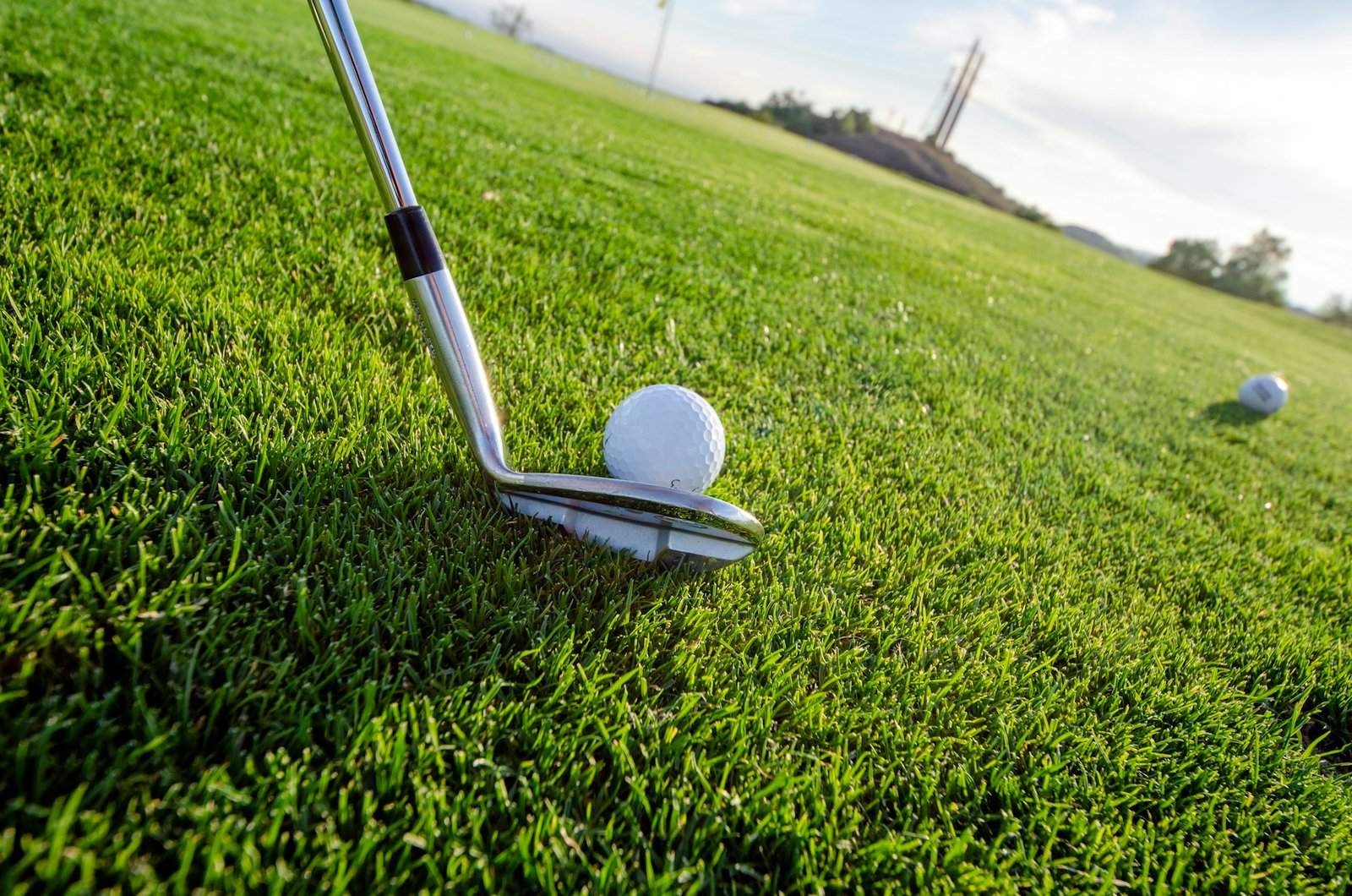 Iron club head set behind a golf ball on short fairway grass