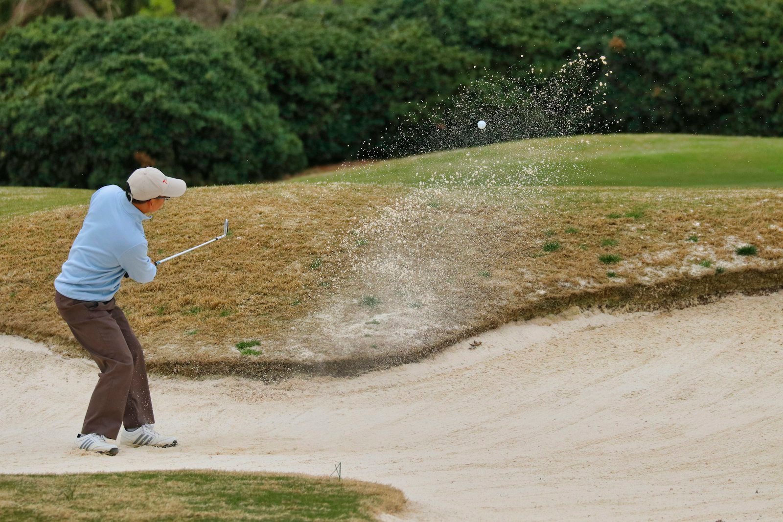 Golfer hitting out of a sand trap with sand spraying around the ball