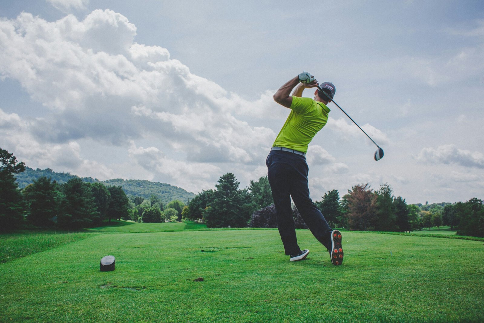 Golfer in a full follow-through on a tee box beside a fairway
