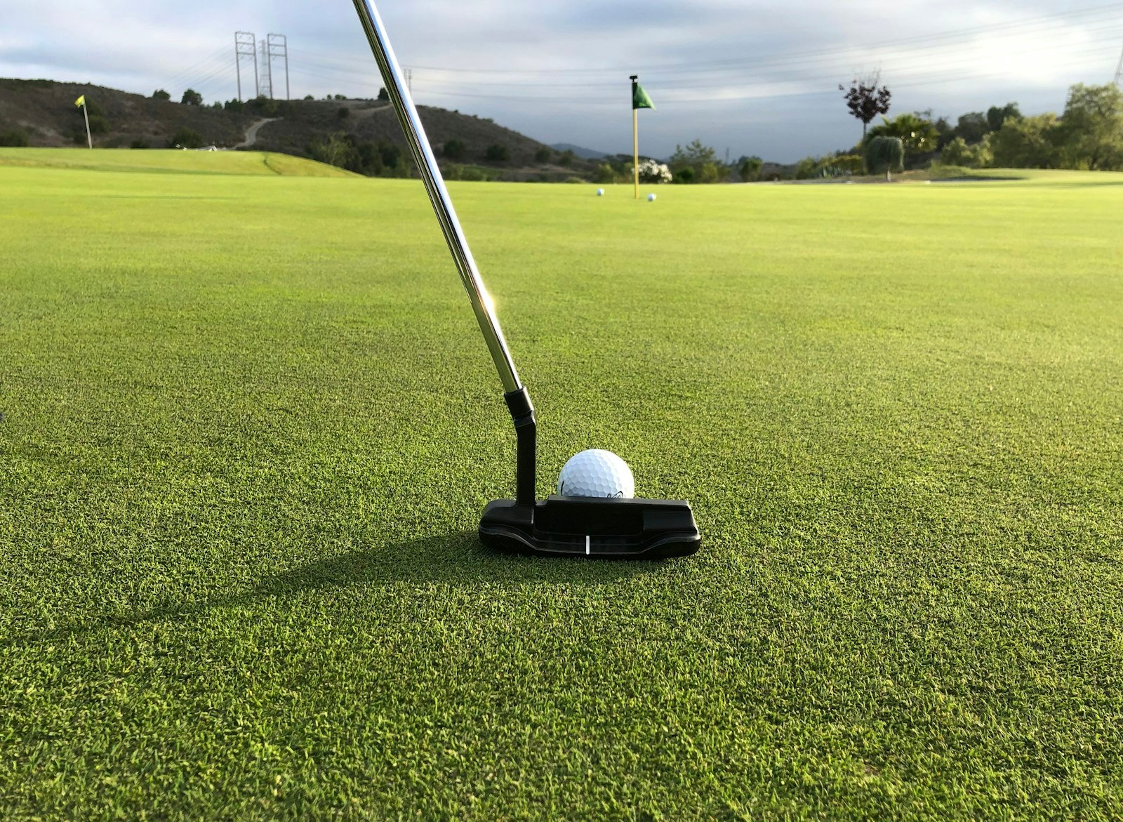 Putter sitting behind a golf ball on the green, ready for the putt that finishes a sandie