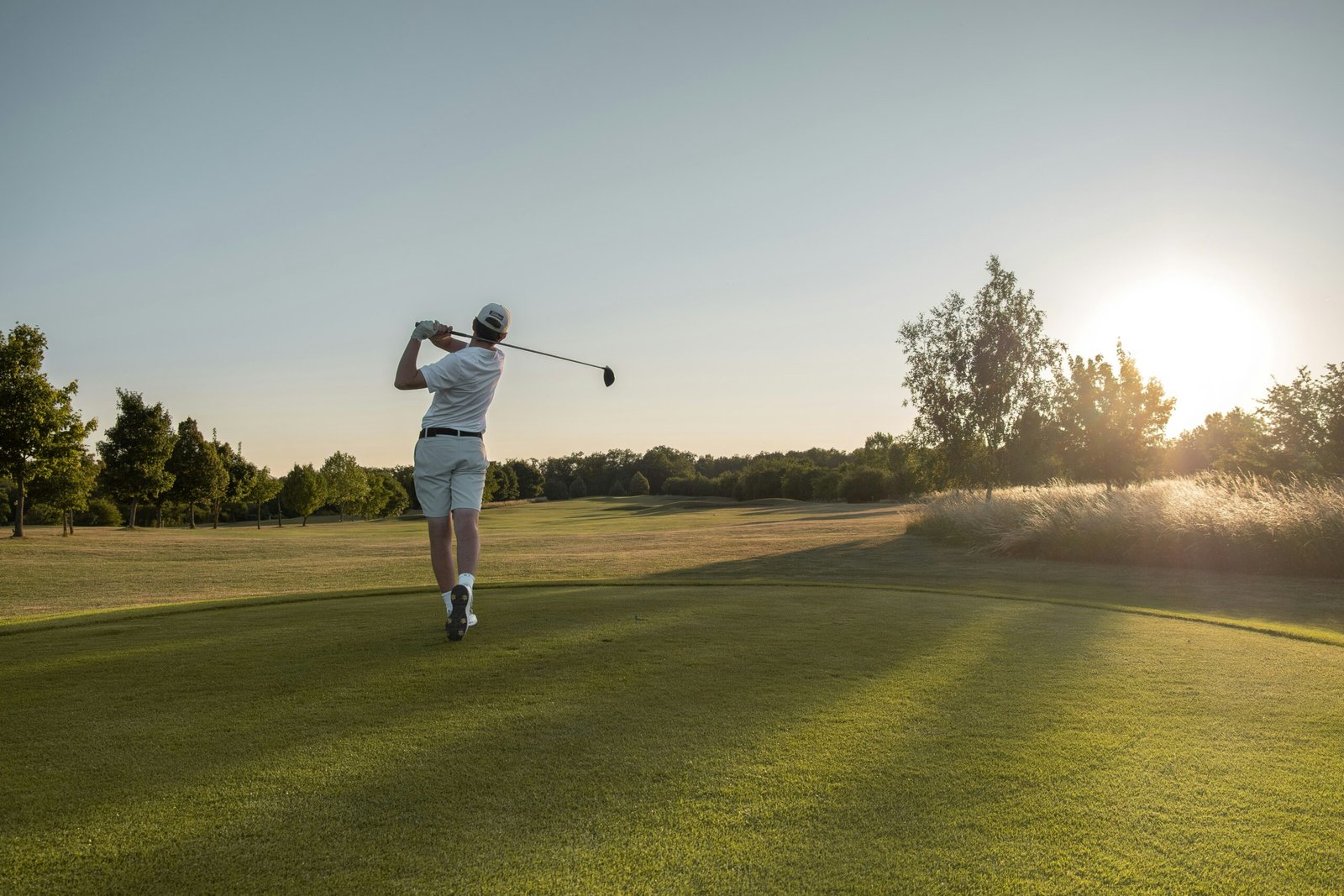 Golfer swinging on a sunny open course at sunset
