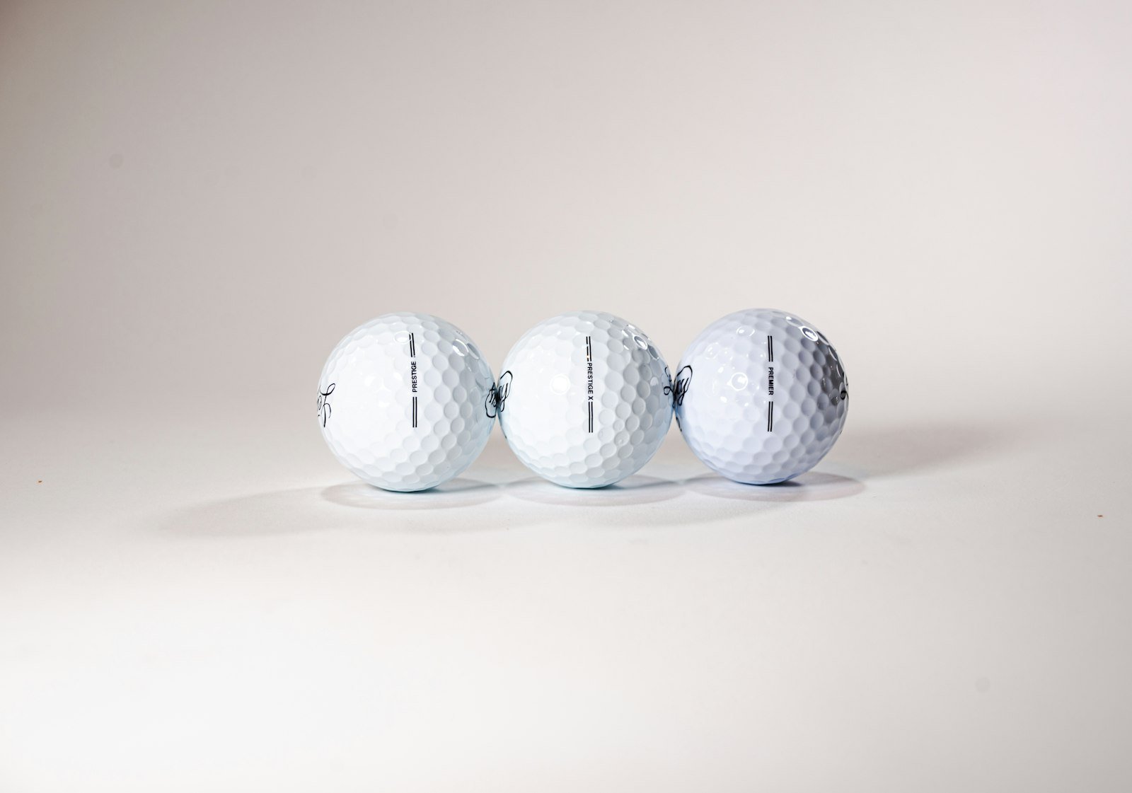 Three new white golf balls lined up in a row on a plain background
