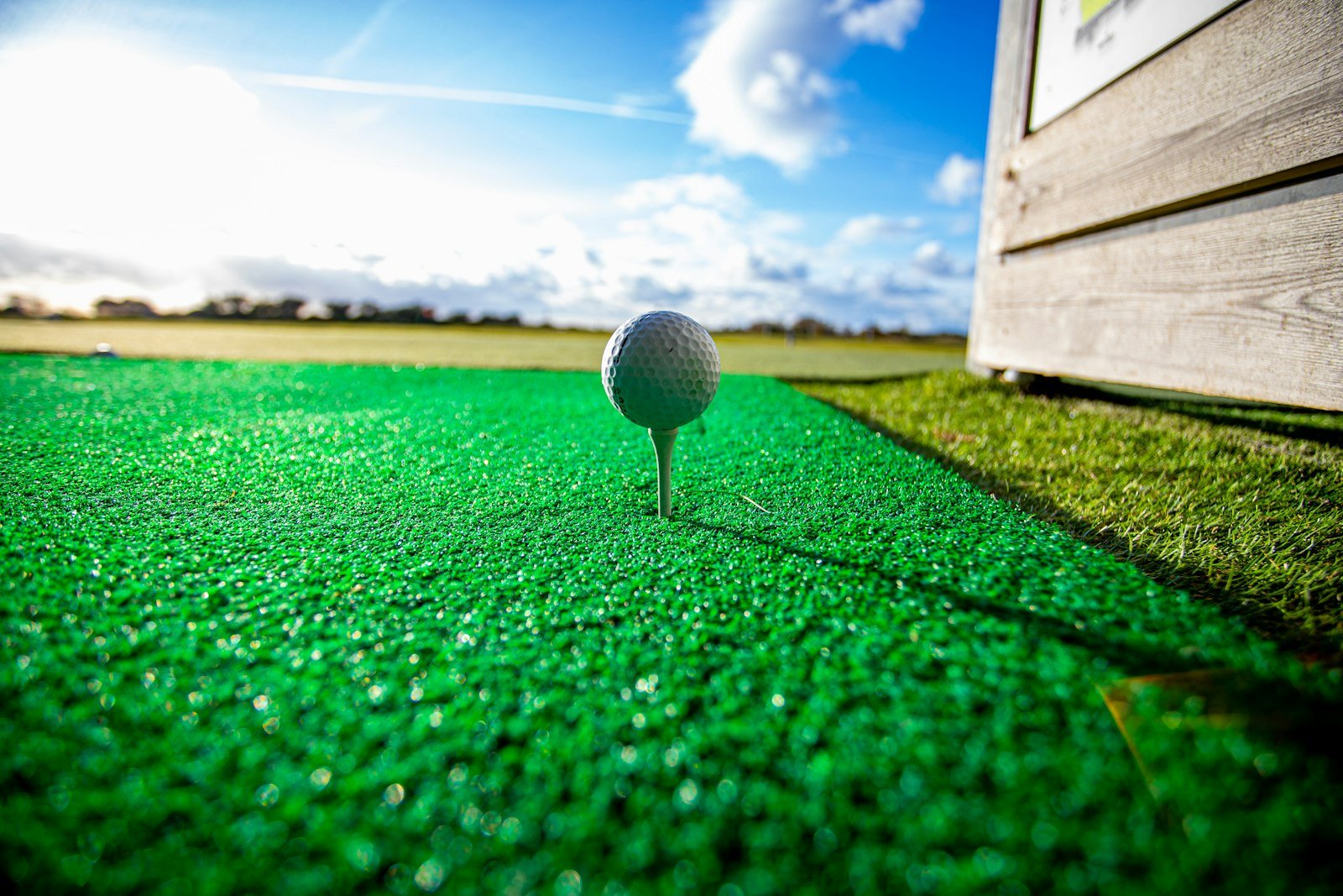White golf ball sitting on a tee on a green practice mat under a blue sky